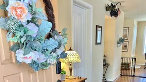 A hallway with a wooden floor, a door with a decorative wreath, a table with a lamp, and a small shelf with a green vase. - Mountain Escape - Pet-Friendly - Fenced Yard - Fast WiFi - Near Flagstaff (Flagstaff)