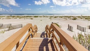 Ein hölzerner Steg führt zu einem Strand bei blauem Himmel.