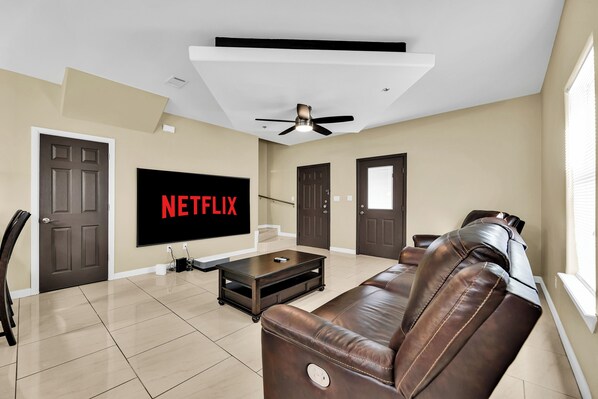 A living room with a brown leather sofa, a flat-screen TV, and a ceiling fan.
