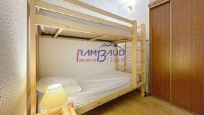 Habitación con literas de madera, colchón blanco, lámpara de noche y armario.