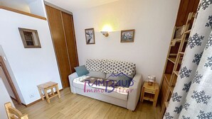 Una habitación pequeña y acogedora con un sofá gris, una mesita de madera, un taburete de madera y un armario de madera.