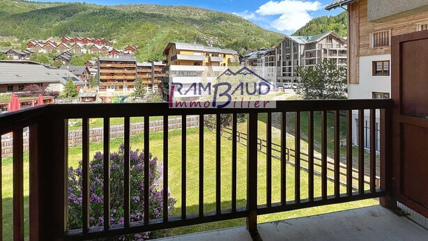 Un balcón con vistas a una zona montañosa, un cartel de 'RAMBAUD Immobiliier' y una valla de madera.