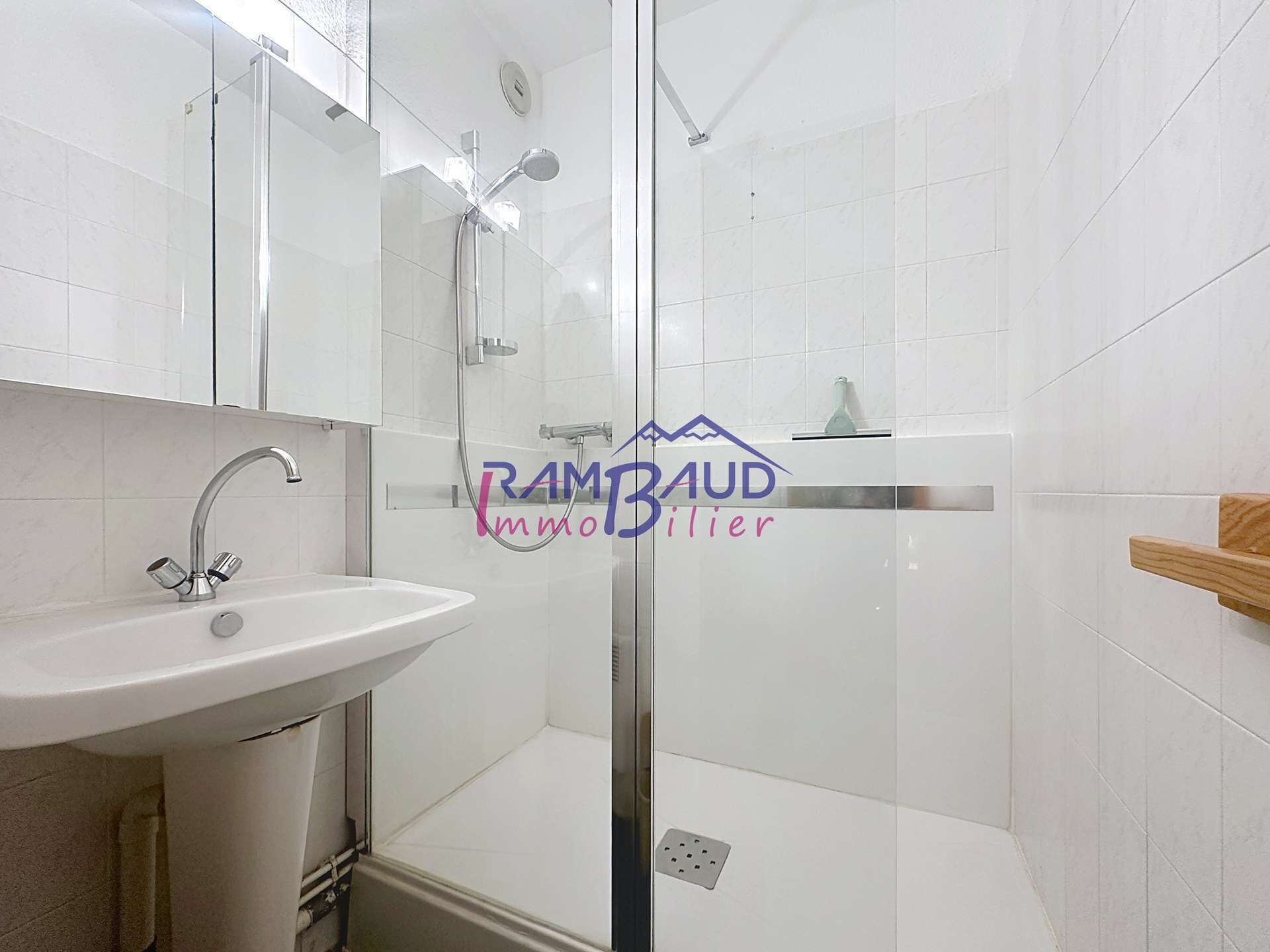 Un baño moderno con cabina de ducha de vidrio, lavamanos blanco y estante de madera.
