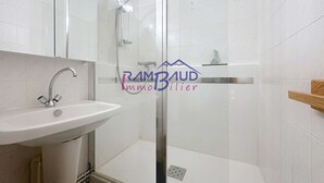 Un baño moderno con cabina de ducha de vidrio, lavamanos blanco y estante de madera.