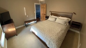 Ein Schlafzimmer mit Bett, Deckenventilator, einer Sitzbank, einem Fernseher und einer Tür zu einem anderen Raum.