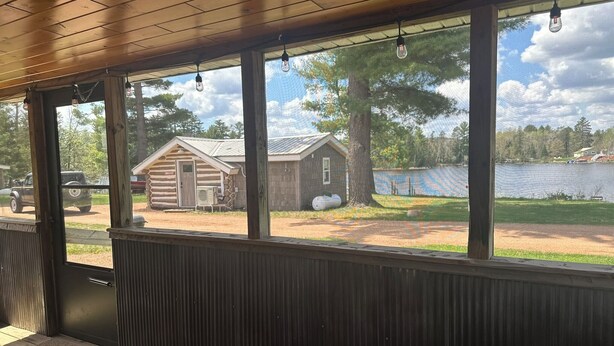 Un porche cubierto con vistas a una cabaña rústica y un lago.