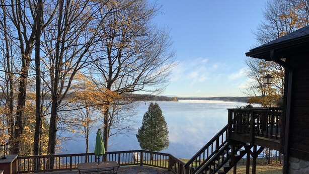 Una terraza junto al lago con una escalera de madera que conduce a un edificio de piedra, rodeado de árboles y vistas al lago.