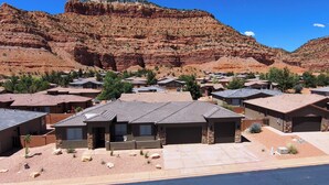 A residential area with houses featuring flat roofs and stone foundations, set against a backdrop of red rock formations. - Modern Luxury Home in Kanab, Utah with Hot Tub & Pool! Near Zion National Park, Bryce Canyon, the Grand Canyon, and the Coral Pink Sand Dunes! (Kanab)