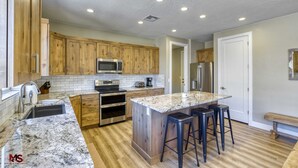 A kitchen with wooden cabinets, a granite countertop, a built-in microwave, a stainless steel refrigerator, and a large island with bar stools. - Modern Luxury Home in Kanab, Utah with Hot Tub & Pool! Near Zion National Park, Bryce Canyon, the Grand Canyon, and the Coral Pink Sand Dunes! (Kanab)