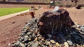 A rock feature with water spouting from it, surrounded by a gravel area and a grassy field. - Modern Luxury Home in Kanab, Utah with Hot Tub & Pool! Near Zion National Park, Bryce Canyon, the Grand Canyon, and the Coral Pink Sand Dunes! (Kanab)