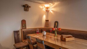 A wooden dining table with four chairs, a vase with flowers, and two glasses of red wine.