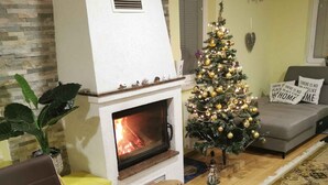 A cozy living room with a fireplace, a Christmas tree, a dining table with a fruit bowl and cookies, and a sofa with decorative pillows. - Holiday house rustically furnished (Dvor)