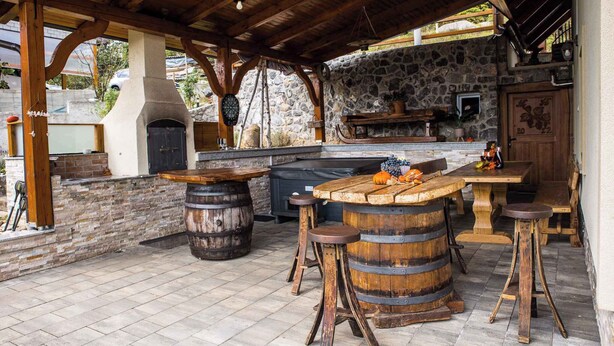 An outdoor kitchen area with a stone wall, wooden tables, and stools. - Holiday house rustically furnished (Dvor)