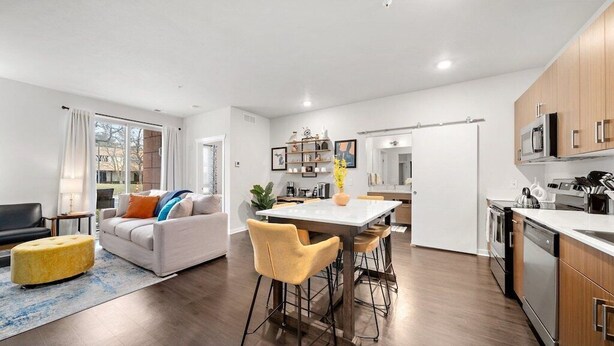 Un salon moderne comprenant un canapé, un pouf et un coin repas avec des chaises et une table.