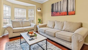 A living room with two beige sofas, a coffee table, and a painting of trees.