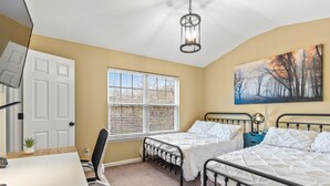 A bedroom with two beds, a desk, a chair, a window, and a painting on the wall.