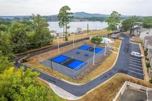A residential area with two blue-roofed swimming pools surrounded by a fence, a parking lot, and a view of a lake and hills in the background.