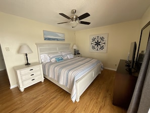 A bedroom with a bed, a nightstand, a lamp, a ceiling fan, a wall clock, and a mirror.