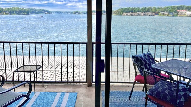 Een balkon met uitzicht op een meer, met metalen hekwerk en buitenmeubilair, waaronder een tafel en stoelen.
