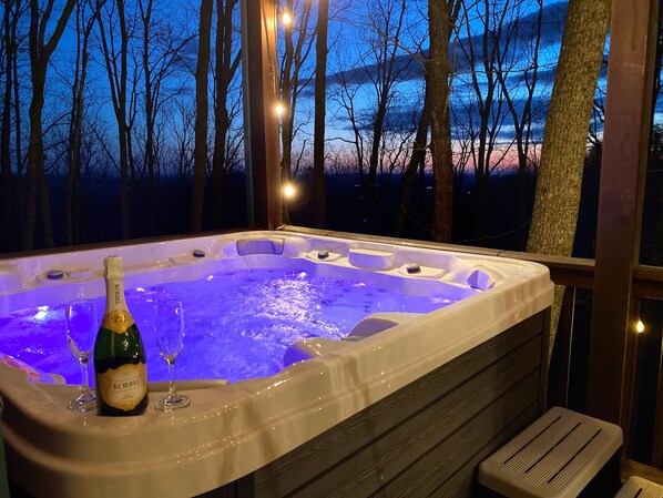 A hot tub with a bottle of Korbel champagne and glasses, surrounded by trees and a wooden deck.