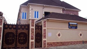 A two-story building with a gated entrance, a signboard advertising serviced apartments, and a brick facade.