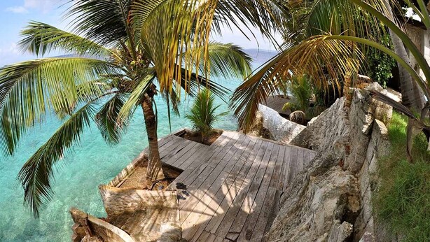 A wooden deck overlooking a clear turquoise sea with palm trees. - Sun Reef Village on Sea (Sint Michiel)