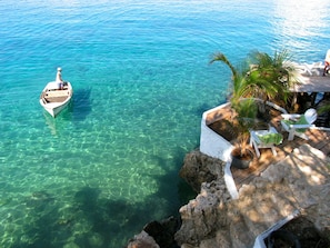 A clear blue sea with a boat and a wooden deck with lounge chairs and a palm tree. - Sun Reef Village on Sea (Sint Michiel)