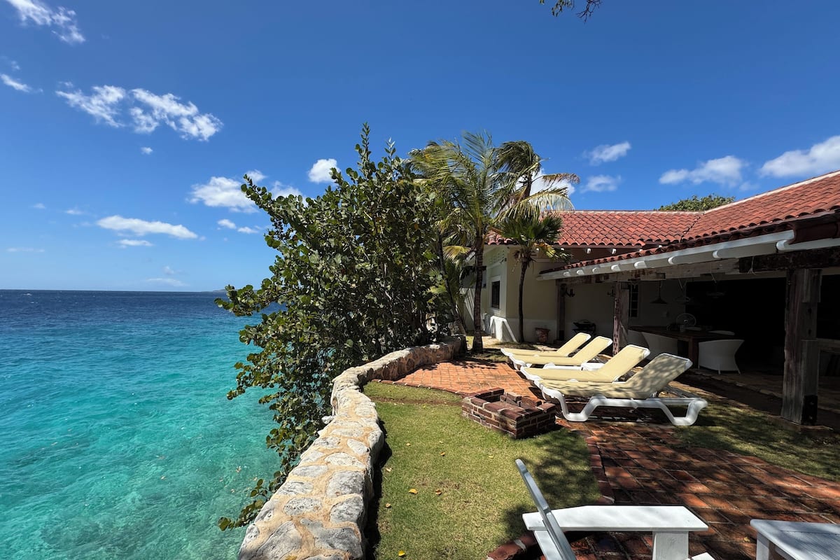 A coastal property with a stone wall, lounge chairs, and a patio overlooking turquoise waters.
