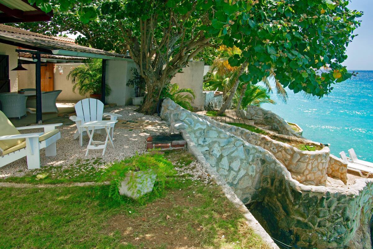 A coastal property with a stone retaining wall, outdoor seating, and a view of the ocean.