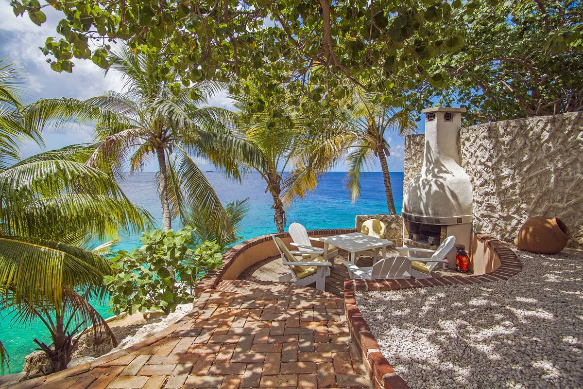 A patio with outdoor furniture, a stone wall, and a view of the ocean.