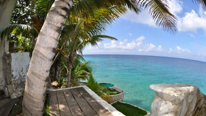 A wooden deck with a view of the ocean, palm trees, and a white wall. - Sun Reef Village on Sea (Sint Michiel)