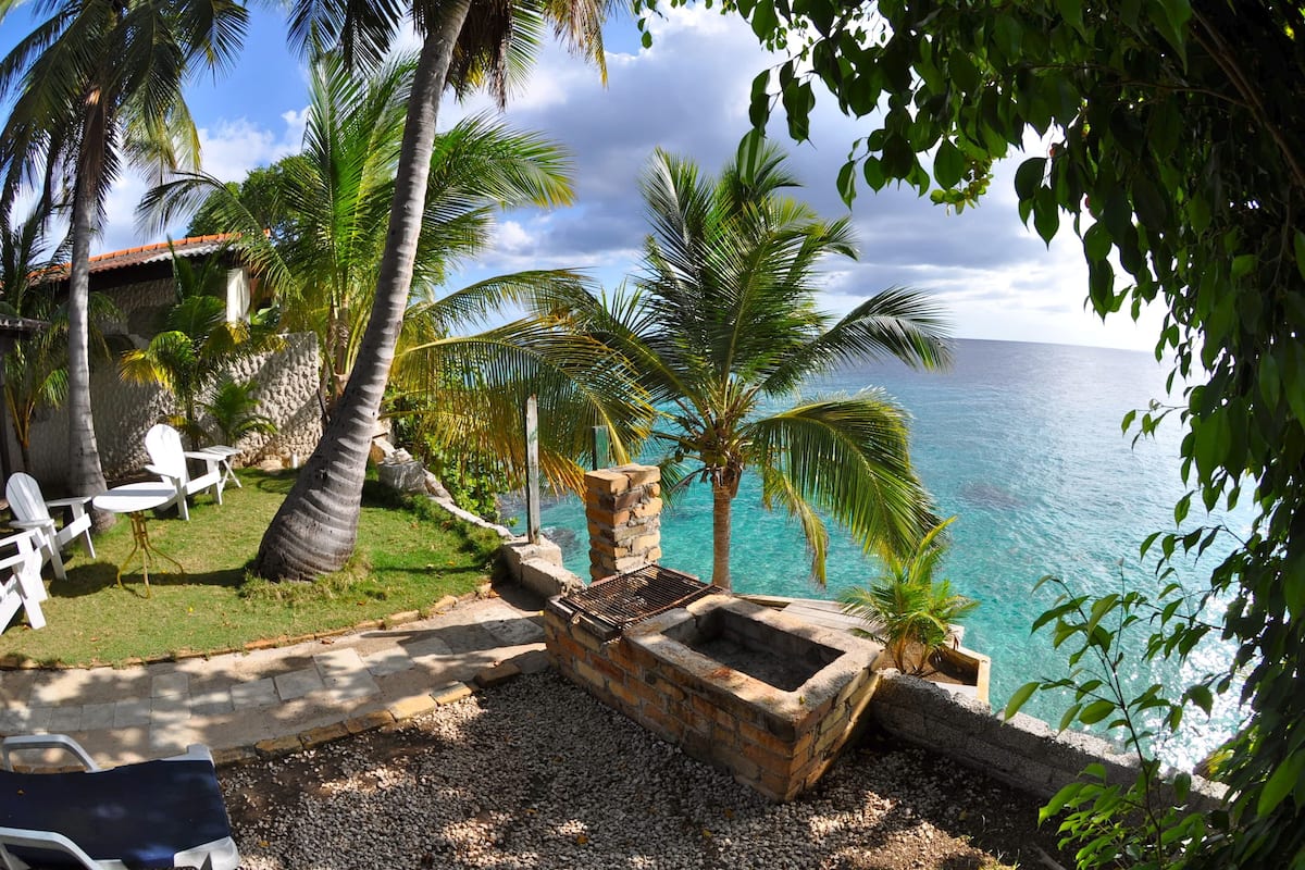A beachside patio with outdoor seating, a stone grill, and a view of the ocean.