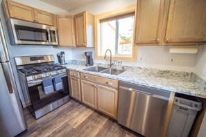 A modern kitchen with stainless steel appliances, wooden cabinets, a granite countertop, and a window providing natural light.