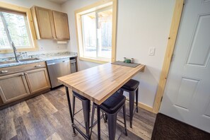 A kitchen with wooden cabinets, a granite countertop, a built-in dishwasher, and a window with a view of trees.