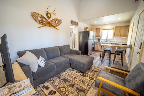 A modern living room with a sectional sofa, a flat-screen TV, and a decorative wall piece.