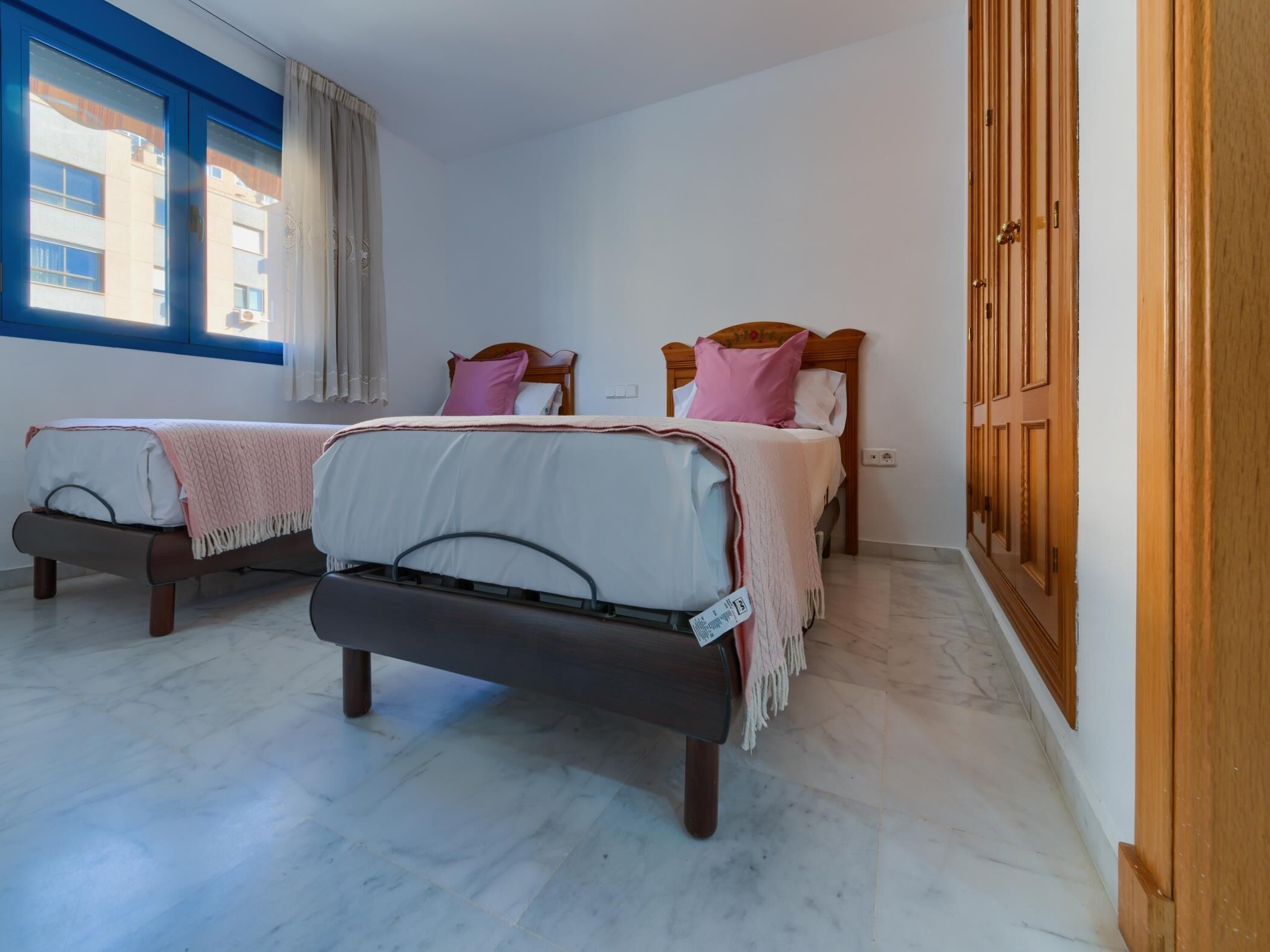 Une chambre d’hôtel avec deux lits, une armoire en bois et une fenêtre avec des rideaux.