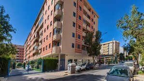 Un hotel de varios pisos con balcones, una entrada porticada y un estacionamiento.