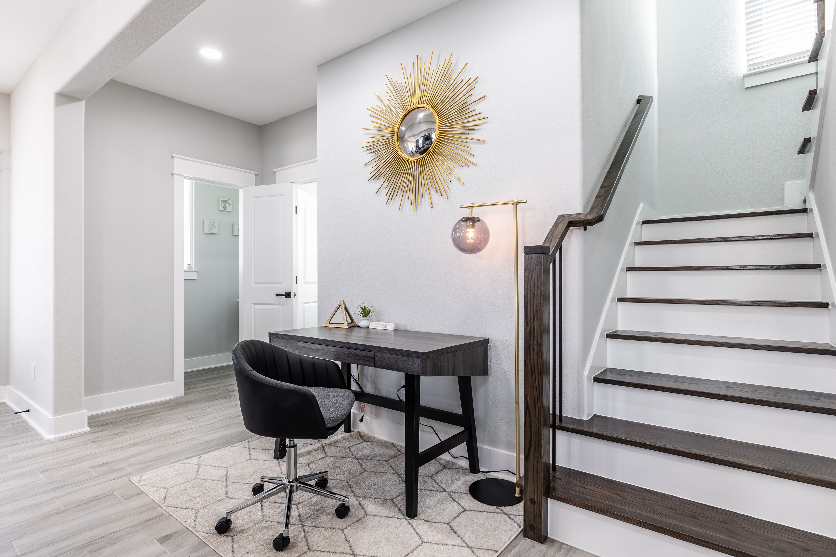 Ein modernes Homeoffice mit Schreibtisch, Stuhl und einem Spiegel mit Sonnenstrahlendesign an der Wand.