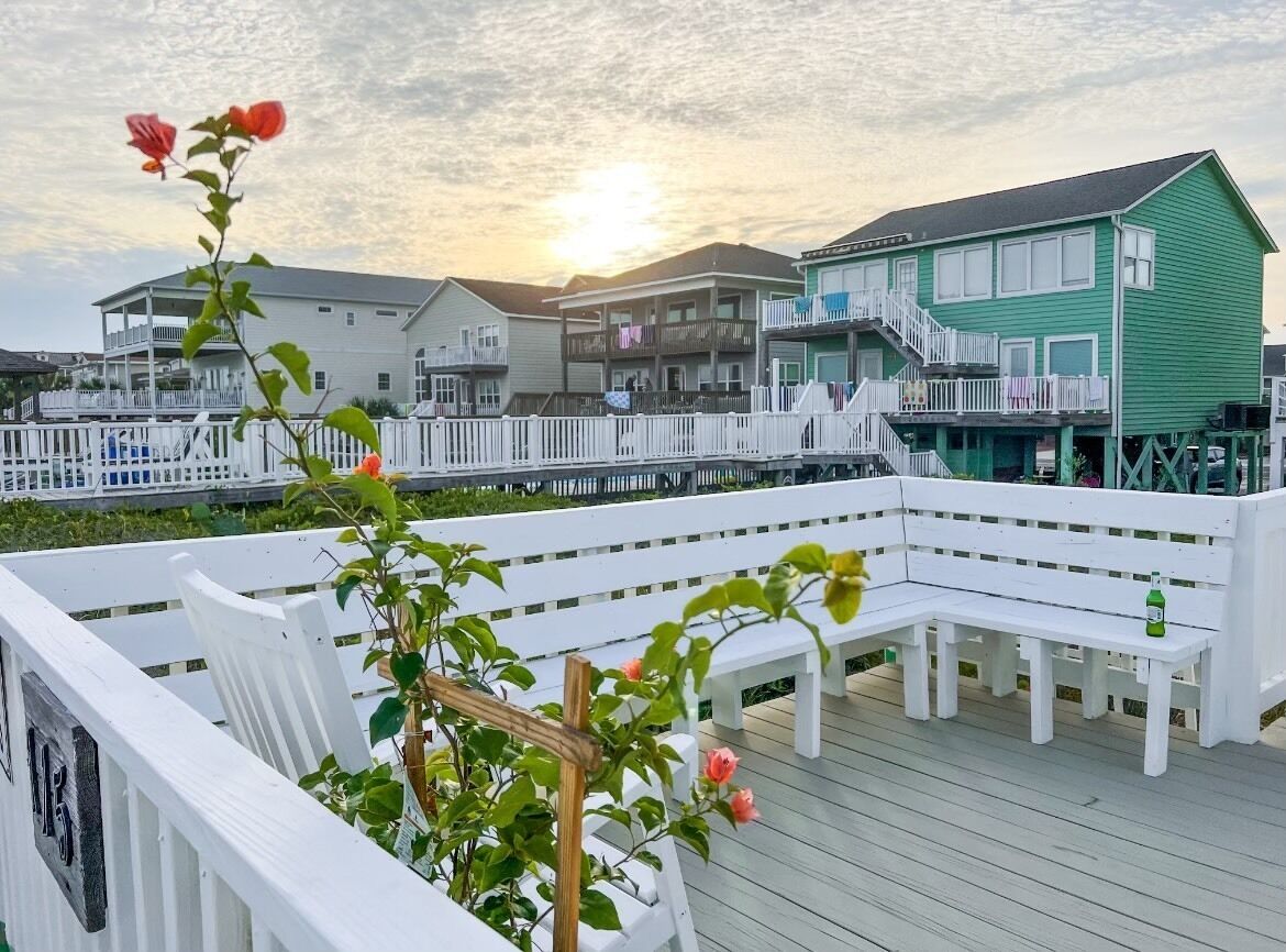 Une terrasse en bois avec des balustrades blanches, un banc et une rangée de maisons en arrière-plan.