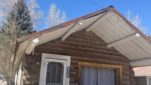 A rustic cabin with a wooden exterior, a white door, and a small porch with red chairs. - THE FRAN - WALK EVERYWHERE IN DOWNTOWN CREEDE! 1 bedroom, 1 bath (SLEEPS 2) (Creede)