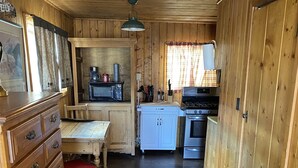 A wooden interior with a kitchen area featuring a microwave, stove, and cabinets. - THE FRAN - WALK EVERYWHERE IN DOWNTOWN CREEDE! 1 bedroom, 1 bath (SLEEPS 2) (Creede)