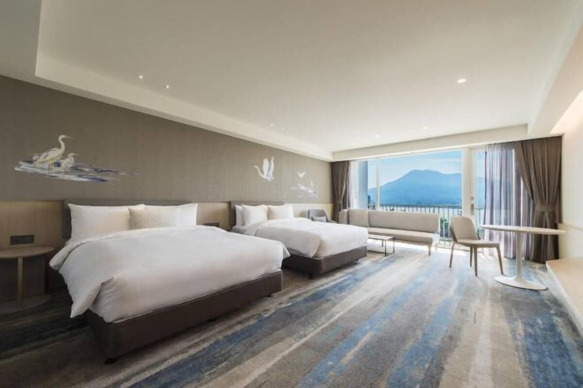 Ein Hotelzimmer mit zwei Betten, einem Schreibtisch, einem Stuhl und einem großen Fenster mit Blick auf die Berge.