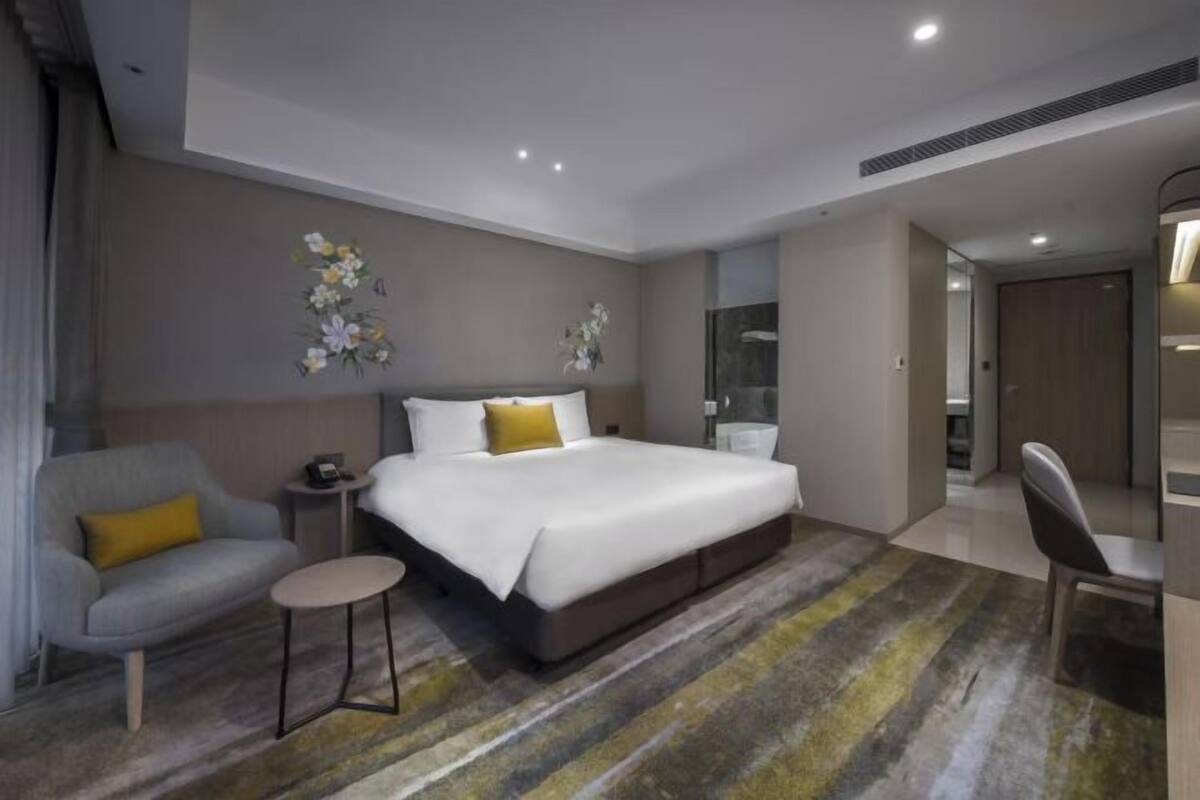 Ein modernes Hotelzimmer mit einem großen Bett, einem kleinen Nachttisch, einem Sessel und einem Spiegel.