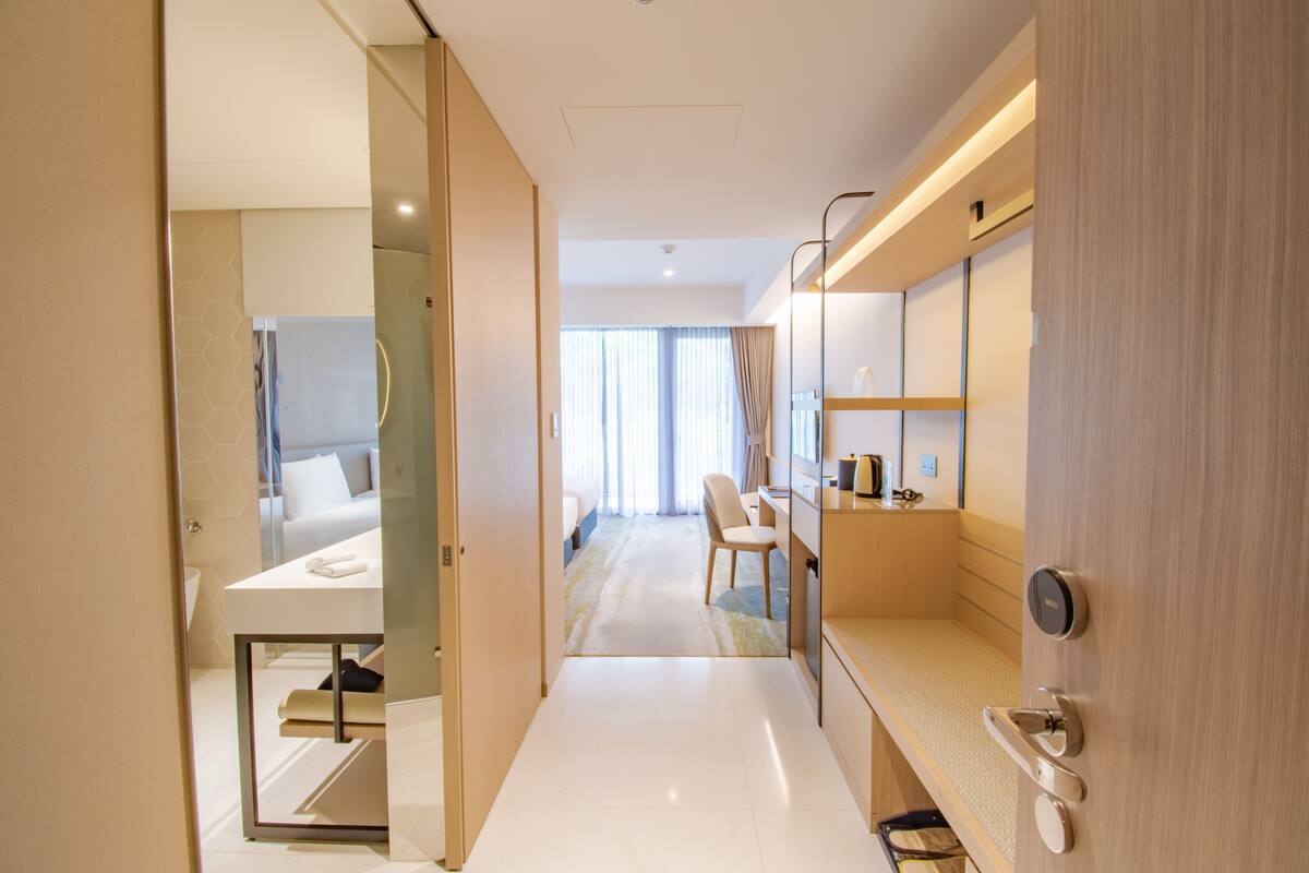 Ein Hotelzimmer mit einem Bett, einem Schreibtisch und einem Stuhl. Es gibt ein Badezimmer mit Toilette und Waschbecken. Das Zimmer verfügt über ein großes Fenster mit Vorhängen.