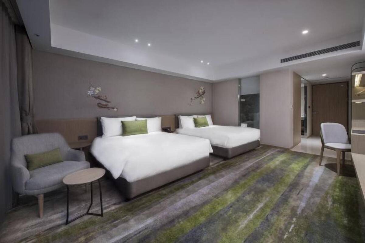 Ein Hotelzimmer mit zwei Betten, einem kleinen runden Tisch, einem Sofa und einem Spiegel.