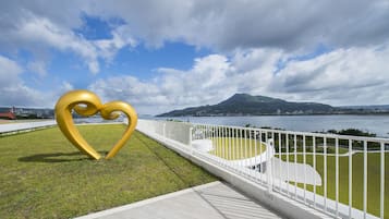 Un parque con una gran escultura dorada en forma de corazón, una valla blanca y una vista de una ciudad y montañas al fondo.