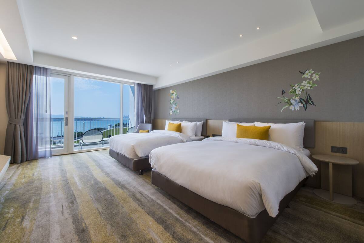 Ein Hotelzimmer mit zwei Betten, einem großen Fenster mit Blick und einem Balkon.