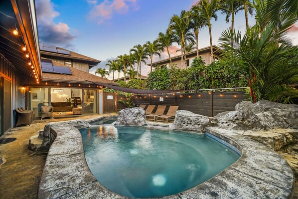 A backyard with a hot tub, lounge chairs, and a pool.