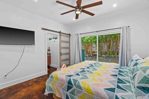 Een slaapkamer met een bed, een plafondventilator, een schuifdeur naar een balkon en uitzicht op groen.