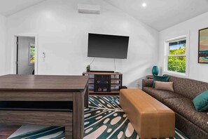A modern living room with a flat-screen TV, a wooden coffee table, a patterned rug, a brown sofa with cushions, and a bookshelf.